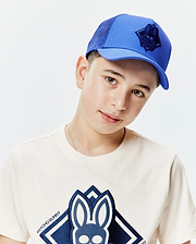 Classic fit cream jersey t-shirt with a large navy blue embroidered Psycho Bunny skull logo on the chest, and a royal blue Kids Tobias Trucker Cap with mesh back and a navy embroidered bunny skull logo.
