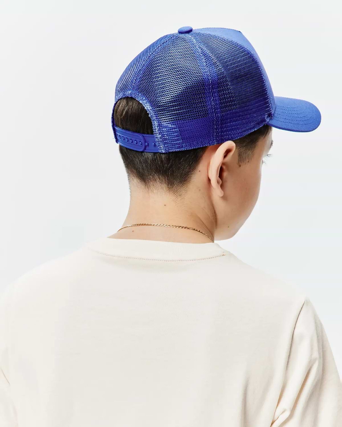 Kids Tobias Trucker Cap, a vibrant royal blue with a structured front panel, breathable mesh back, and adjustable snapback closure, worn with a soft, relaxed-fit cream jersey t-shirt.