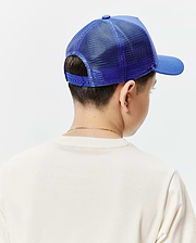 Kids Tobias Trucker Cap, a vibrant royal blue with a structured front panel, breathable mesh back, and adjustable snapback closure, worn with a soft, relaxed-fit cream jersey t-shirt.