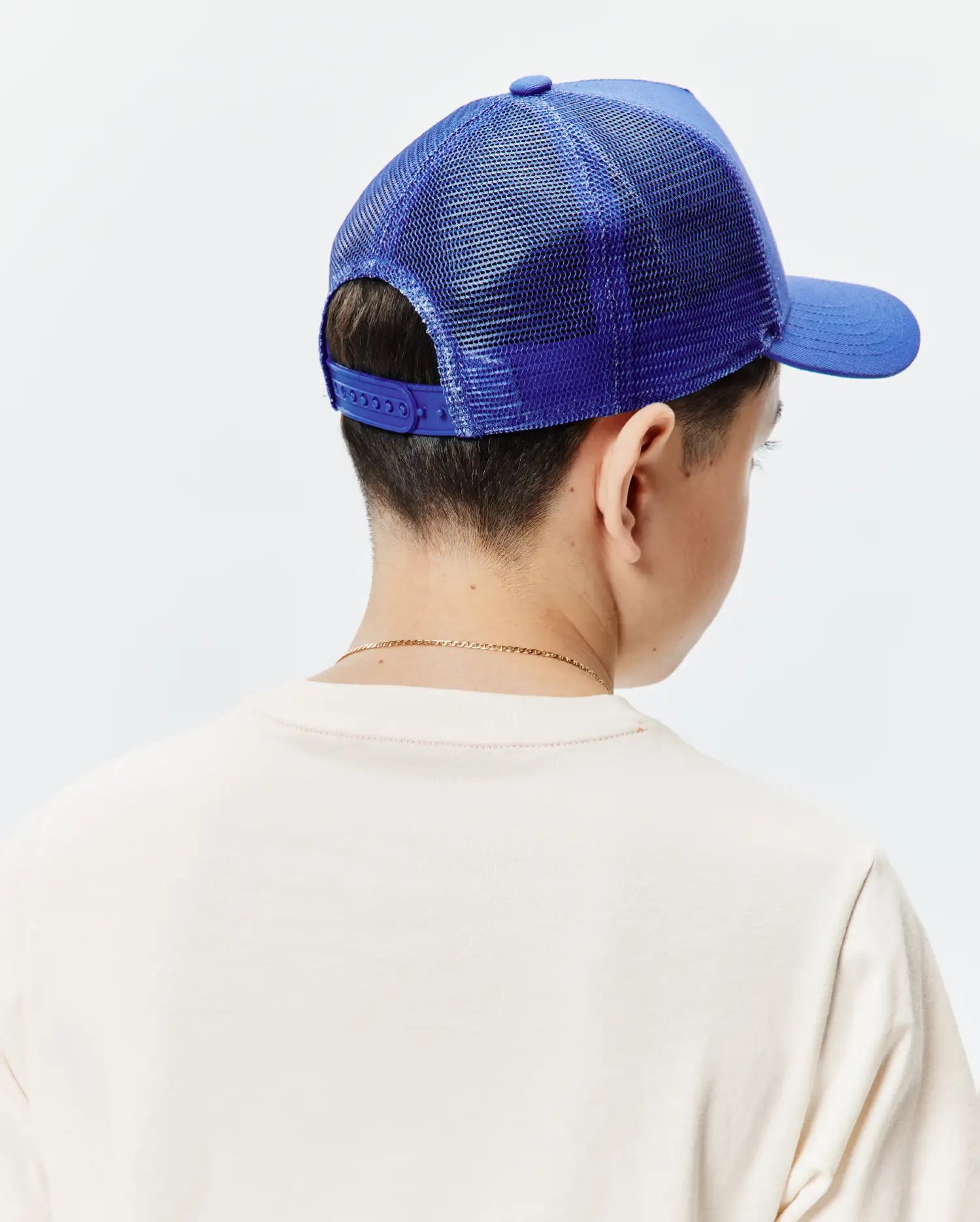Kids Tobias Trucker Cap, a vibrant royal blue with a structured front panel, breathable mesh back, and adjustable snapback closure, worn with a soft, relaxed-fit cream jersey t-shirt.