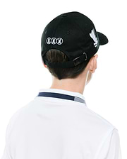 Black Kids Nathaniel A-Frame Trucker Cap with white embroidered Psycho Bunny skull logos on back and side, metal logo buckle, paired with a white polo featuring a navy and white striped collar.