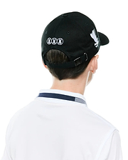 Black Kids Nathaniel A-Frame Trucker Cap with white embroidered Psycho Bunny skull logos on back and side, metal logo buckle, paired with a white polo featuring a navy and white striped collar.