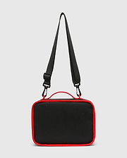 Kids Pal Lunch Box, sleek black durable fabric with vibrant red piping, a sturdy top handle, and an adjustable black shoulder strap featuring red carabiner clips.