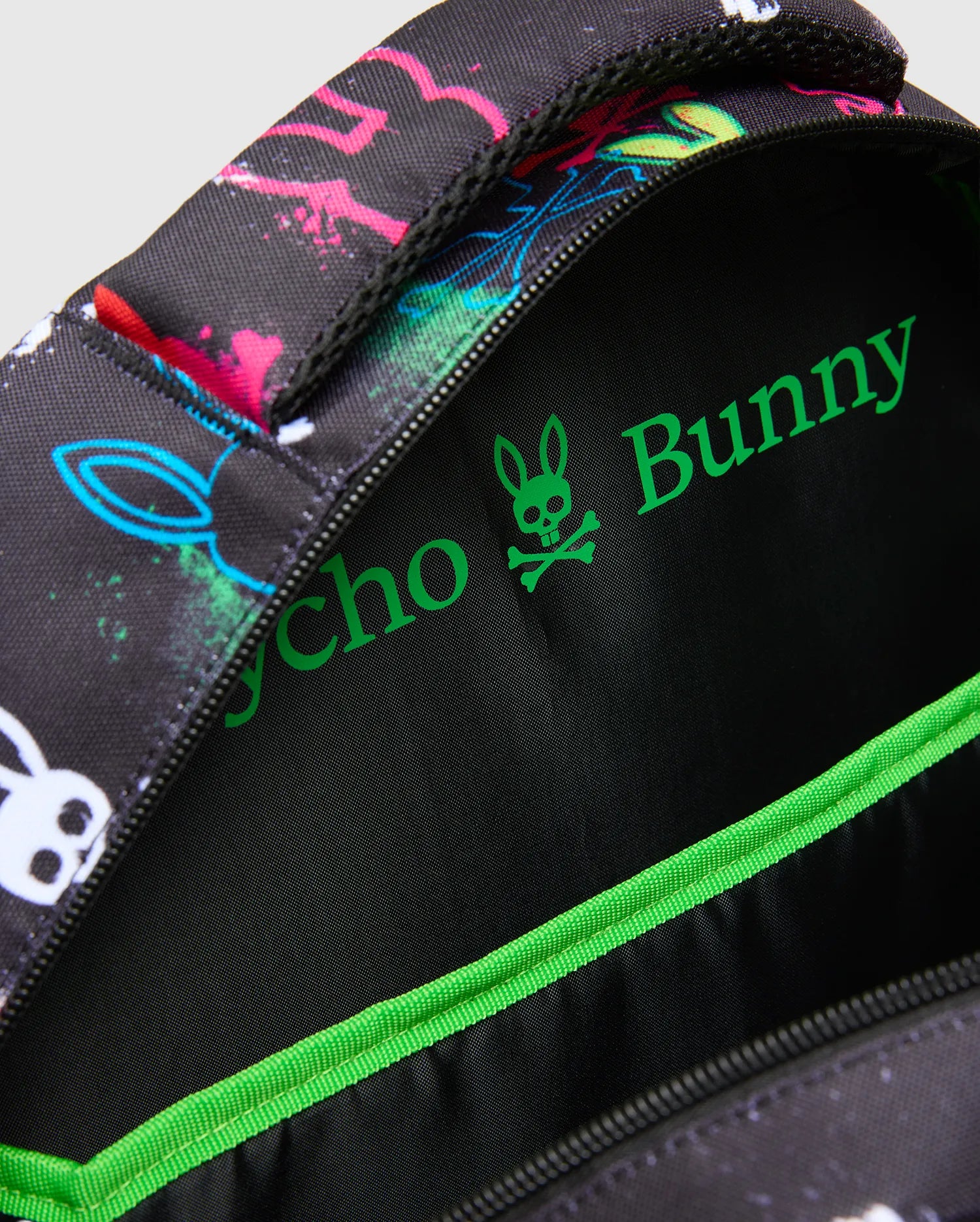 Kids Quintin Backpack in black with vibrant neon pink, blue, green, and white splatter bunny skull graphics, featuring a bright green Psycho Bunny logo and trim on the interior.