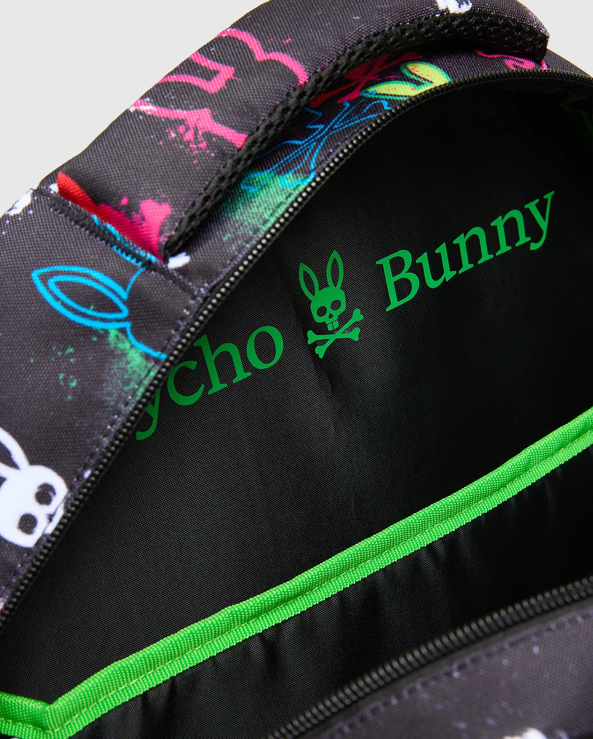 Kids Quintin Backpack in black with vibrant neon pink, blue, green, and white splatter bunny skull graphics, featuring a bright green Psycho Bunny logo and trim on the interior.