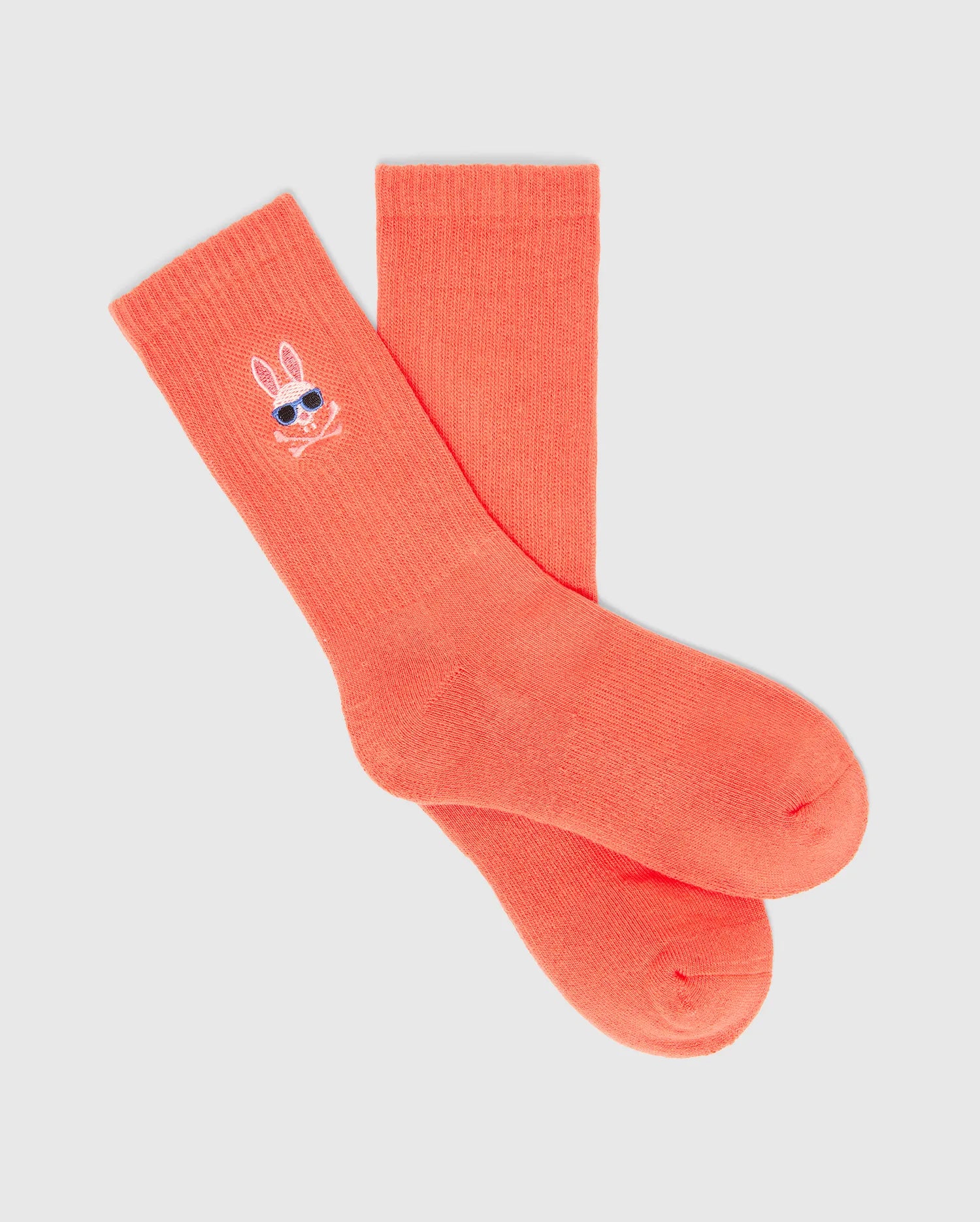 Kids Sunny 3 Pack Sport Socks in vibrant coral, featuring a small embroidered Psycho Bunny skull logo with blue sunglasses on the ribbed cuff, offering a comfortable sport knit texture.