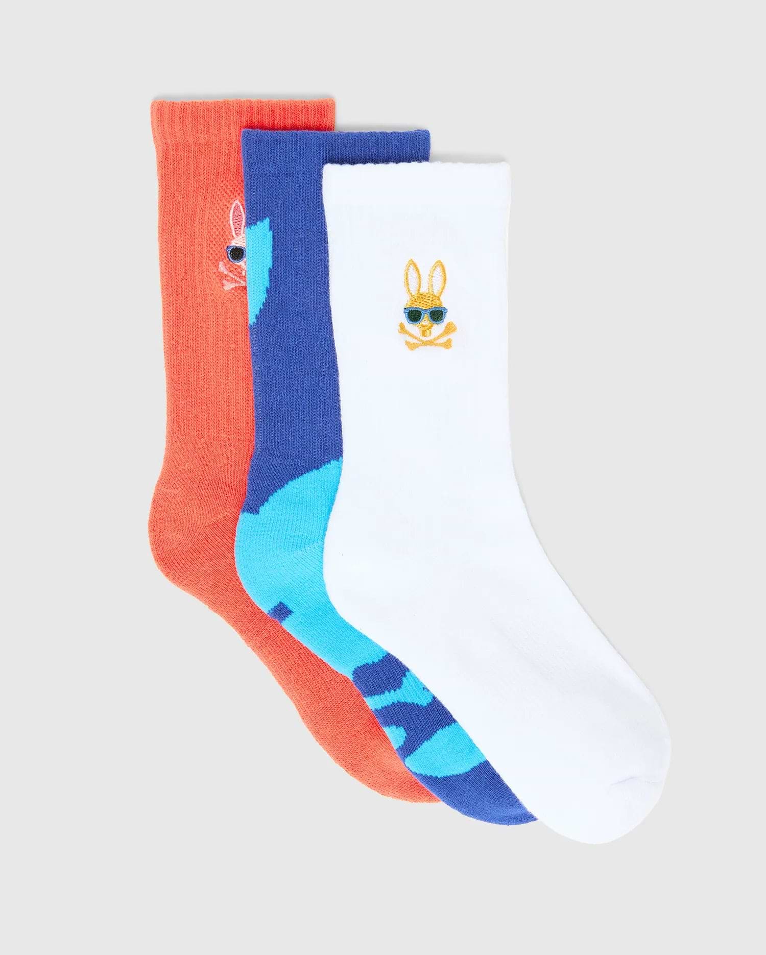 Kids Sunny 3 Pack Sport Socks: a coral ribbed knit, a royal blue and light blue patterned knit, and a white knit sock. Each features a small embroidered Psycho Bunny skull logo, the white one with blue sunglasses.