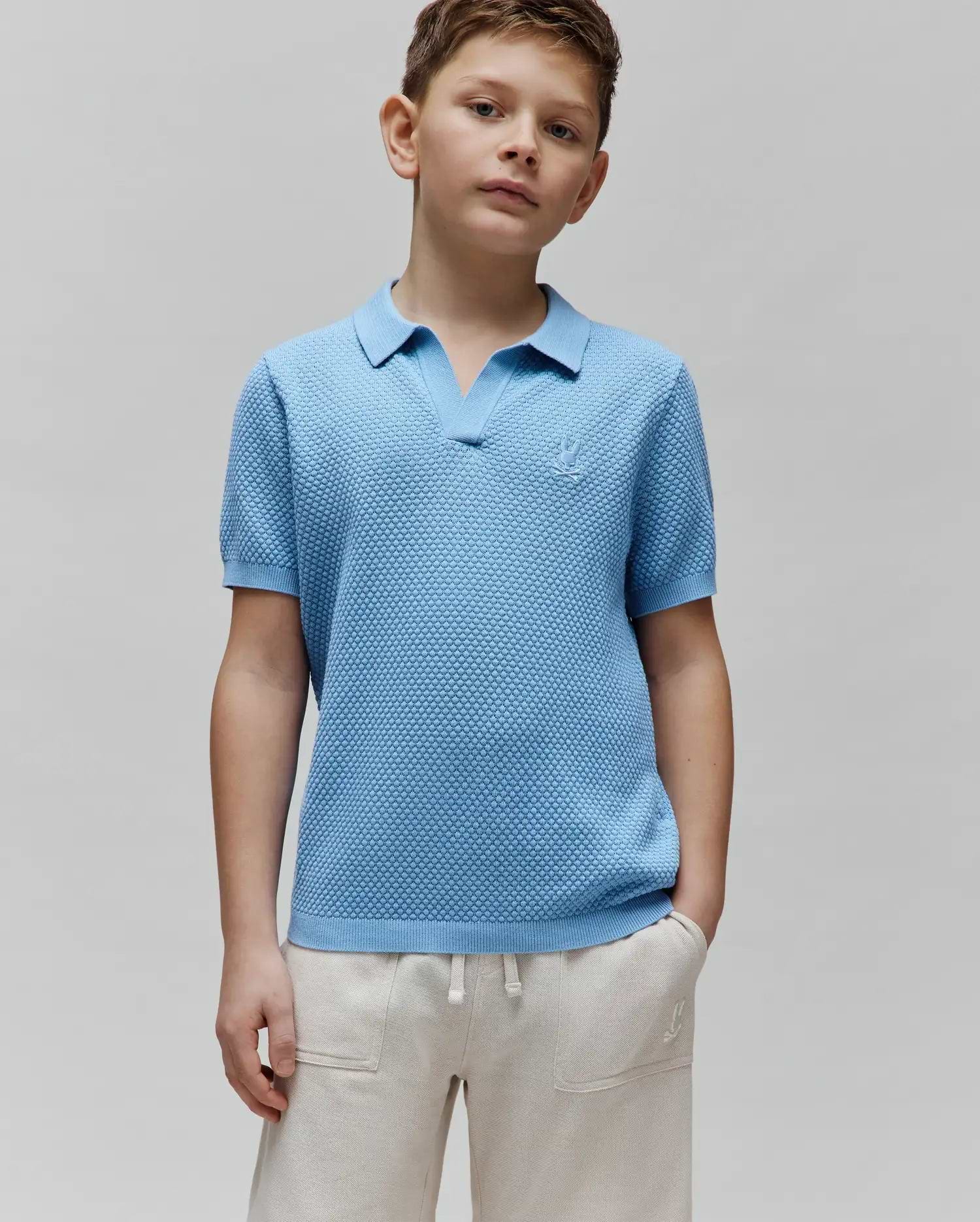 Kids Devon Bubble Stitch Knit Polo in light blue, a classic fit with an open V-neck collar, ribbed cuffs, and a small embroidered Psycho Bunny skull logo on the left chest.