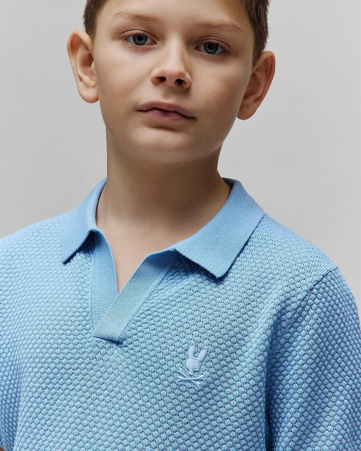 Kids Devon Bubble Stitch Knit Polo in light blue, featuring a textured bubble knit fabric, open V-neck collar, and a small, tone-on-tone embroidered Psycho Bunny skull logo on the left chest.