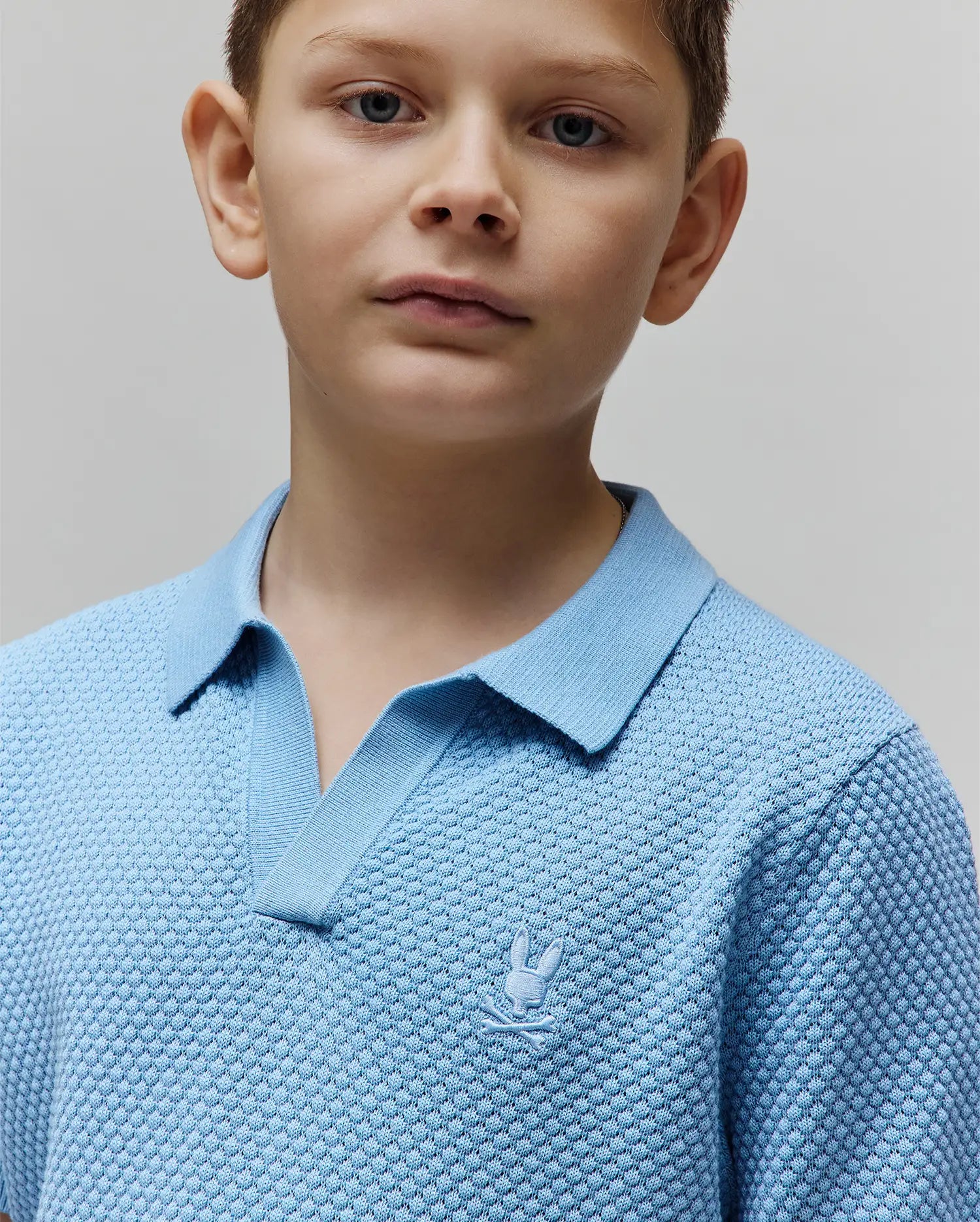 Kids Devon Bubble Stitch Knit Polo in light blue, featuring a textured bubble knit fabric, open V-neck collar, and a small, tone-on-tone embroidered Psycho Bunny skull logo on the left chest.