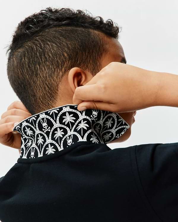 Kids Brad Pique Polo in classic black, featuring a textured pique fabric and a bold, contrasting white pattern on the collar with repeating palm trees and iconic Psycho Bunny skull logos. (2)