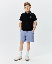 Kids Sunny Pique Polo, black pique with white and blue striped collar/cuffs, white embroidered Psycho Bunny skull logo left chest. Blue heathered shorts with blue embroidered Psycho Bunny logo right leg.