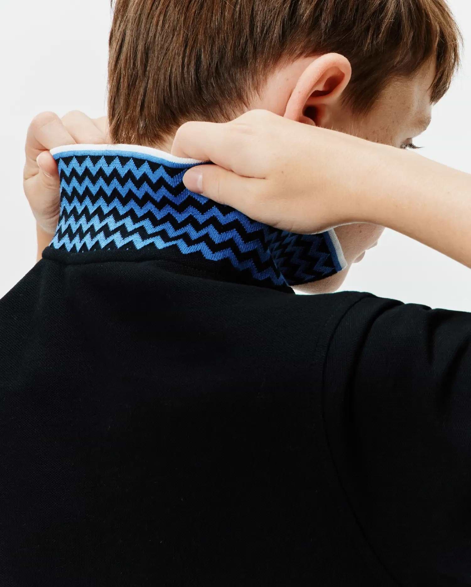 Kids Sunny Pique Polo, a classic fit black pique polo shirt with a bold blue and light blue zigzag pattern on the collar, accented by a crisp white trim.