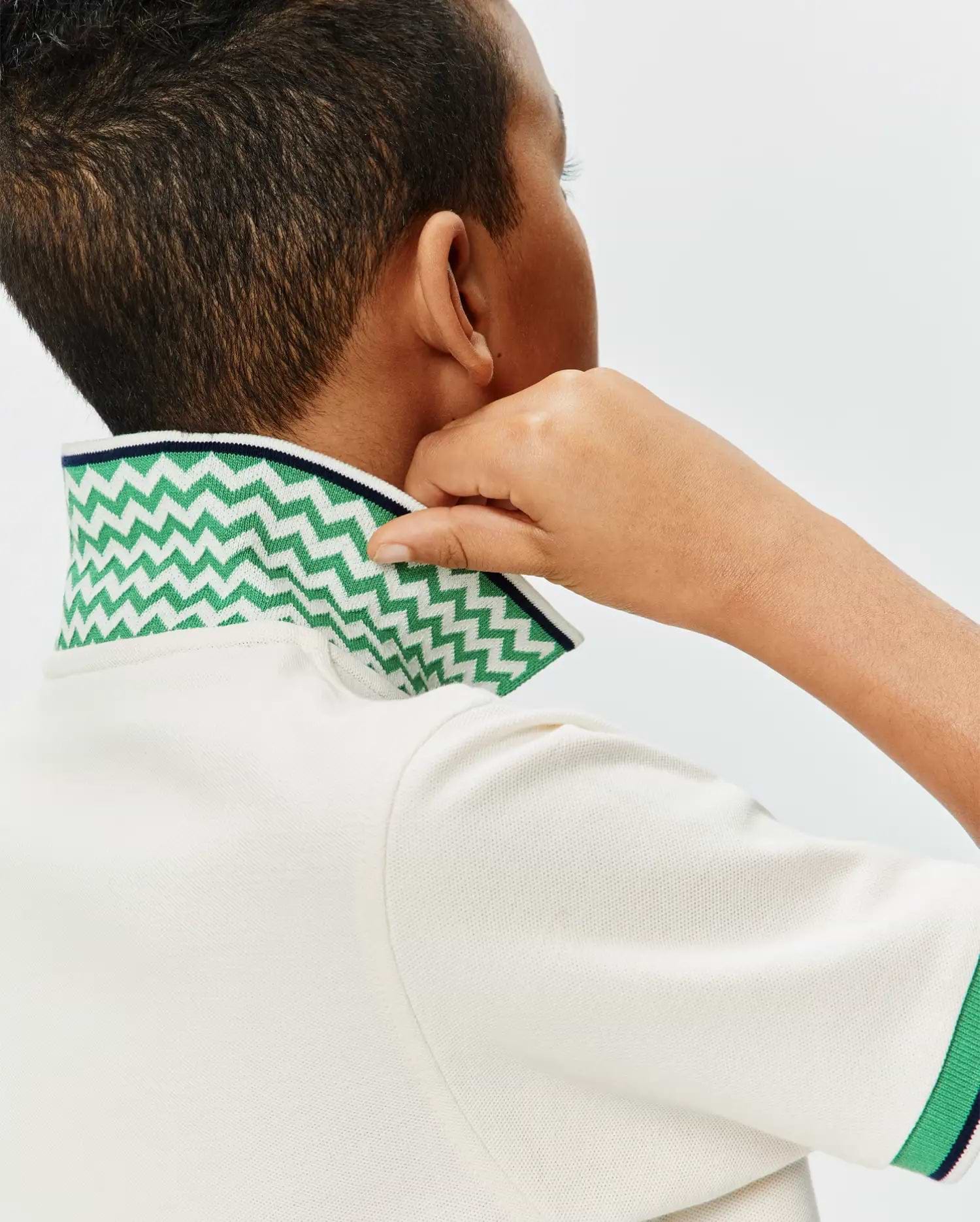 Kids Sunny Pique Polo in cream pique fabric, featuring a bold green and white chevron pattern on the collar with a navy trim, and matching green and navy striped cuffs.
