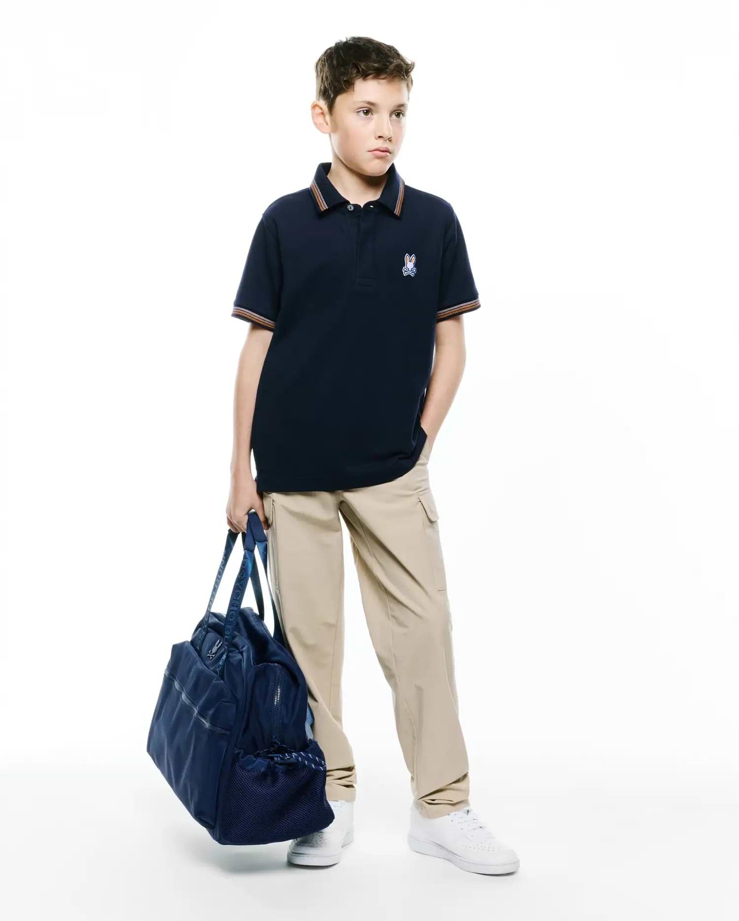 Kids Jaydon Pique Polo in navy blue, featuring a classic fit, textured pique fabric, and a small embroidered Psycho Bunny skull logo on the left chest, with orange and white striped collar and cuffs.