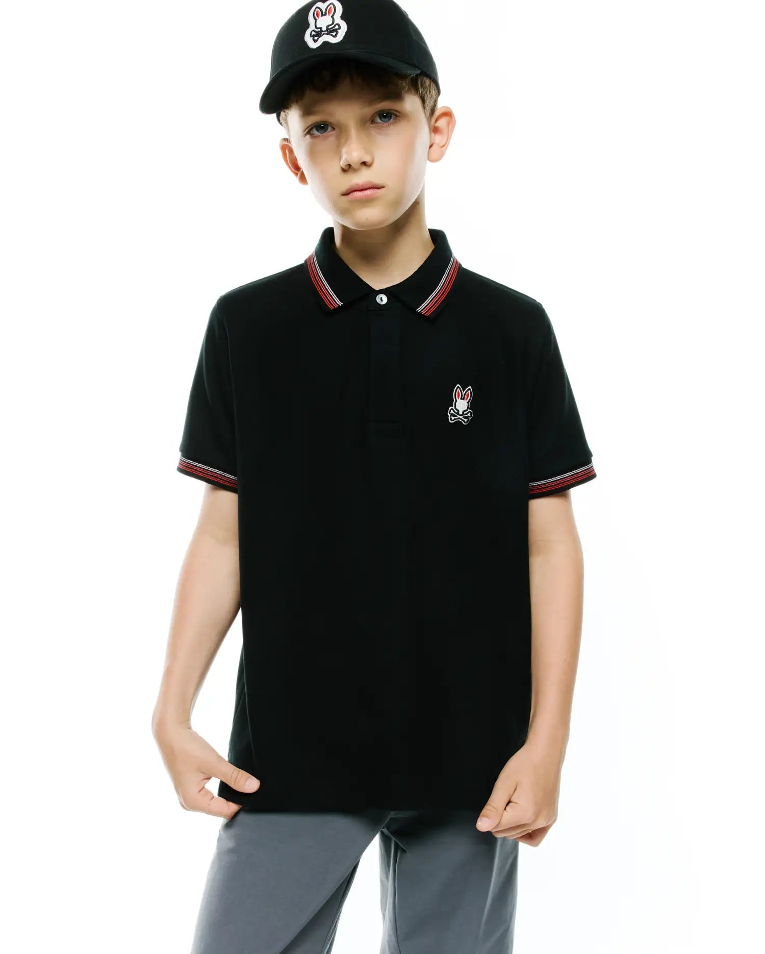 Kids Jaydon Pique Polo, black classic fit pique polo with red and white striped collar and cuffs, featuring a small embroidered Psycho Bunny skull logo on the left chest.