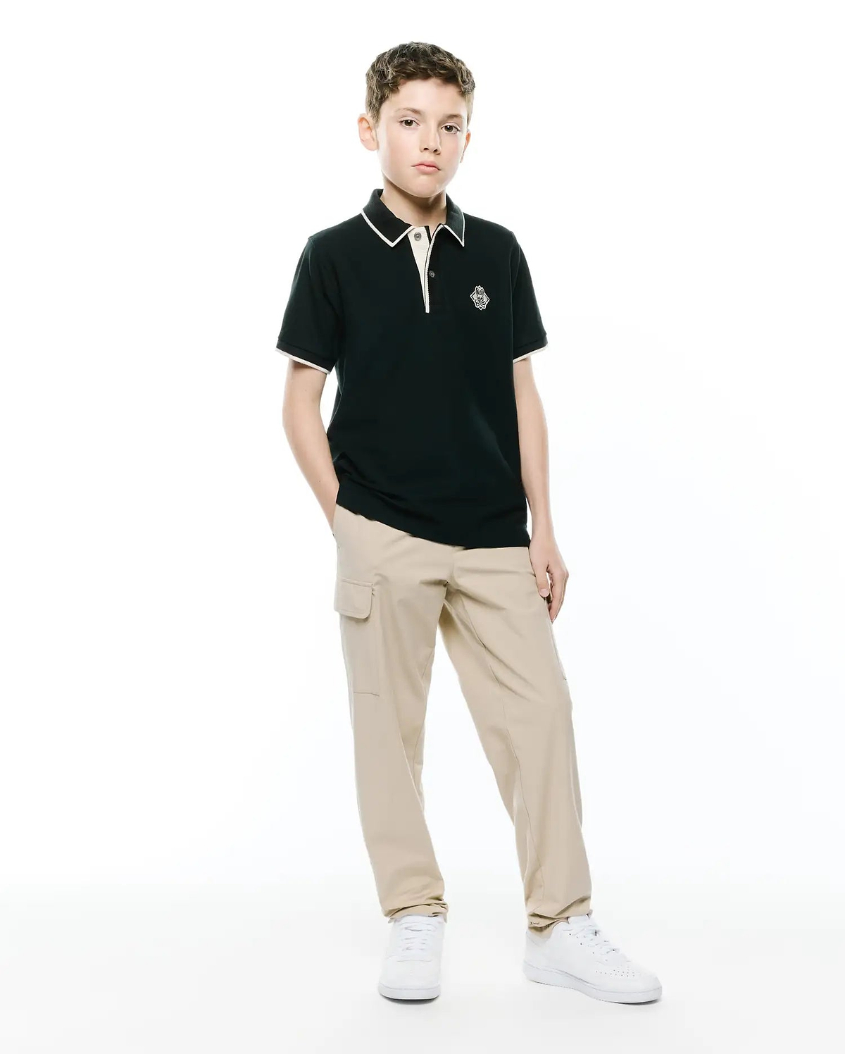 Kids Robin Pique Polo, a classic fit dark green pique polo with white/cream tipping on the collar and cuffs, featuring an embroidered Psycho Bunny skull logo on the left chest.