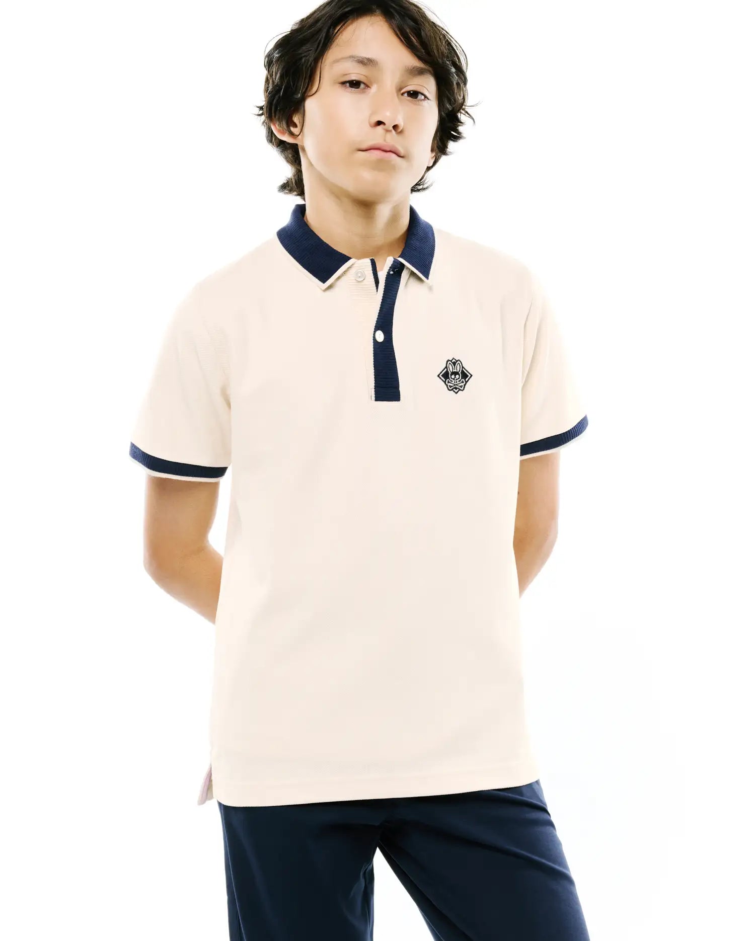 Kids Robin Pique Polo in cream, featuring a classic fit, navy blue ribbed collar and two-button placket, navy blue ribbed sleeve cuffs, and a small embroidered Psycho Bunny skull logo on the left chest.