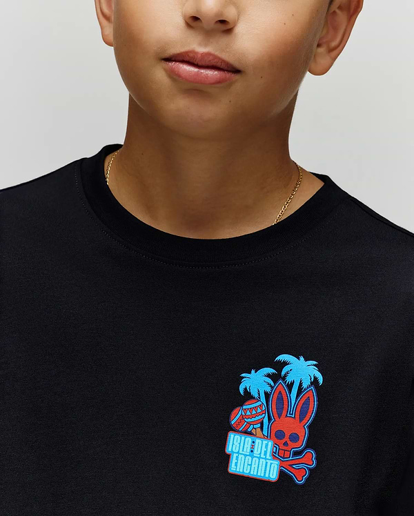 A child wears the Psycho Bunny KIDS PUERTO RICO TEE (KT0200133), a soft black Pima cotton shirt featuring vibrant blue palms, a red skull bunny graphic, and "Isla Del Encanto" text—embodying Puerto Rico’s lively spirit.