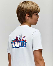 A young boy with light brown hair wears the Psycho Bunny KIDS PUERTO RICO TEE (KT0200133), a white Pima cotton shirt with colorful Puerto Rico-themed graphics and back text, standing against a plain light background.