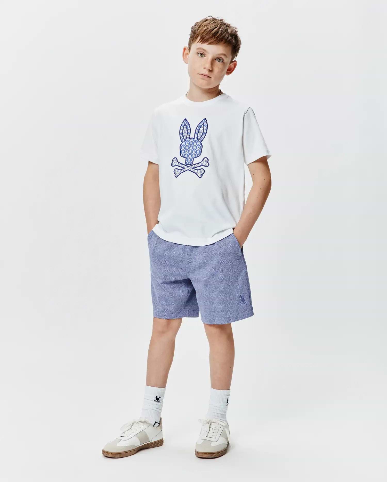 Kids Brad Graphic Tee, a white jersey tee with a large ornate blue Psycho Bunny skull graphic, paired with heather blue relaxed knit shorts featuring a small embroidered bunny logo.