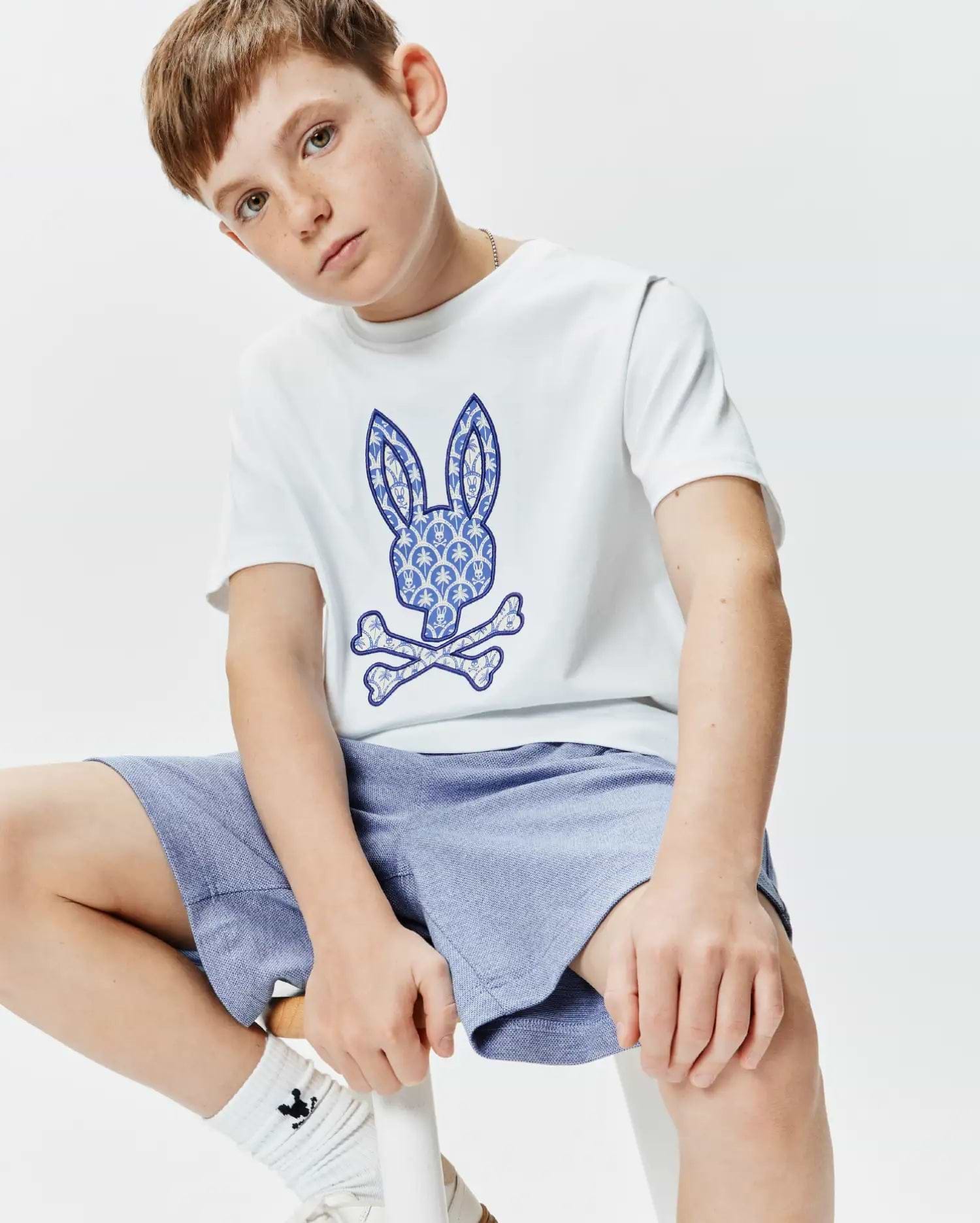 White Kids Brad Graphic Tee, classic fit jersey, with a large blue and white palm tree patterned Psycho Bunny skull and crossbones logo on the center chest.