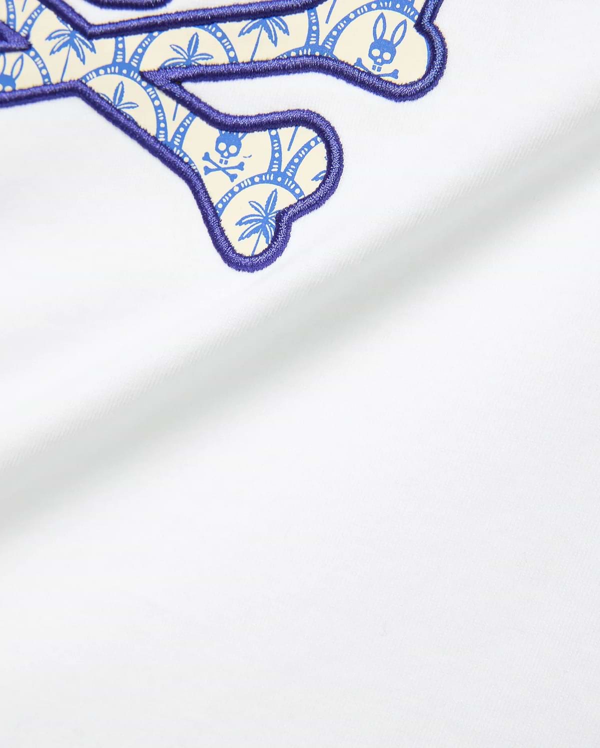 Kids Brad Graphic Tee in white jersey fabric, featuring a large embroidered Psycho Bunny logo with a purple outline and a cream-blue palm tree and skull pattern fill.