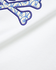 Kids Brad Graphic Tee in white jersey fabric, featuring a large embroidered Psycho Bunny logo with a purple outline and a cream-blue palm tree and skull pattern fill.