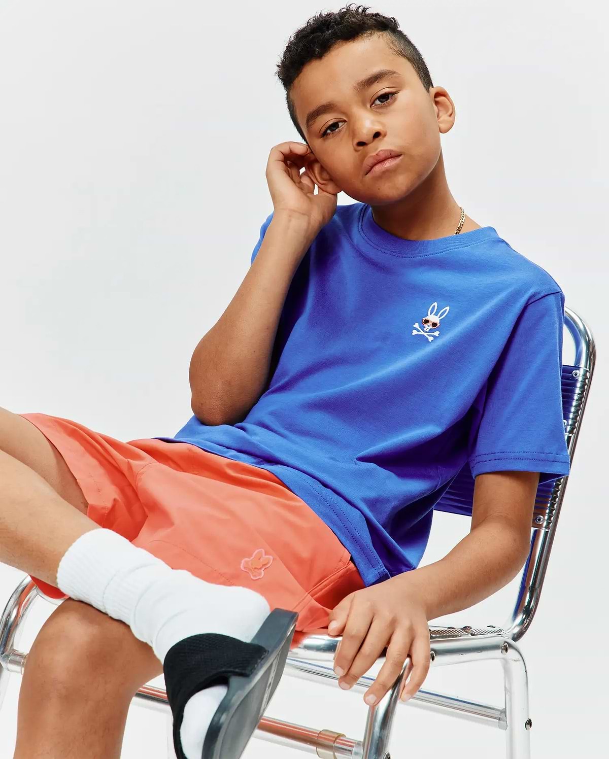 Kids Sunny Chest Graphic Tee, a royal blue jersey tee with a small embroidered Psycho Bunny skull logo wearing sunglasses on the left chest, paired with coral relaxed fit shorts featuring a subtle embroidered bunny.