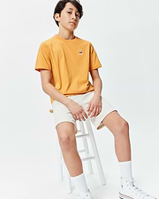 Kids Sunny Chest Graphic Tee in sunny yellow, featuring a classic fit and smooth jersey fabric. It has a small embroidered Psycho Bunny skull logo with red sunglasses on the left chest, paired with cream relaxed-fit shorts.