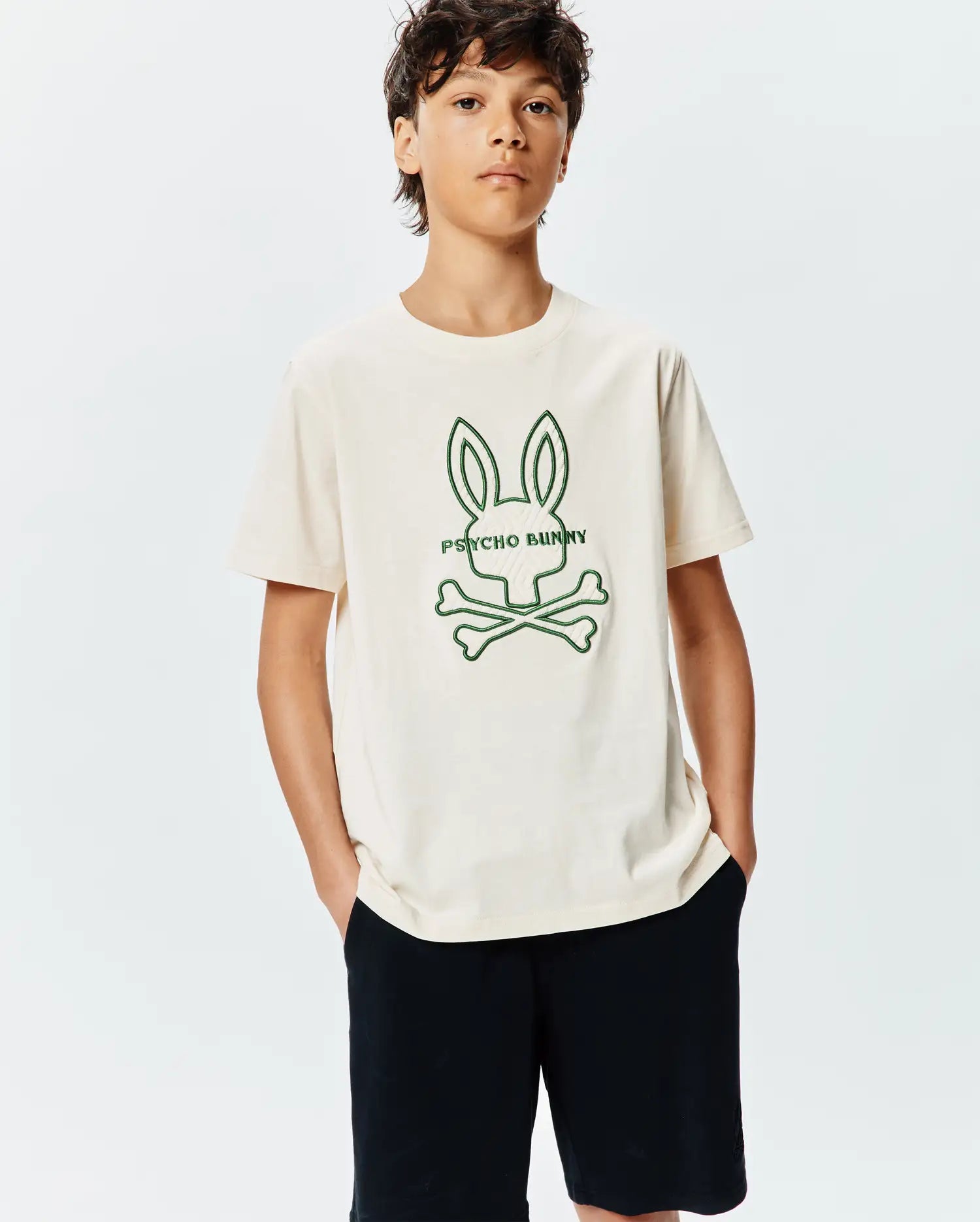 Kids Craig Graphic Tee in cream jersey, featuring a large central green outline of the iconic Psycho Bunny skull and crossbones logo with PSYCHO BUNNY text, in a classic fit.