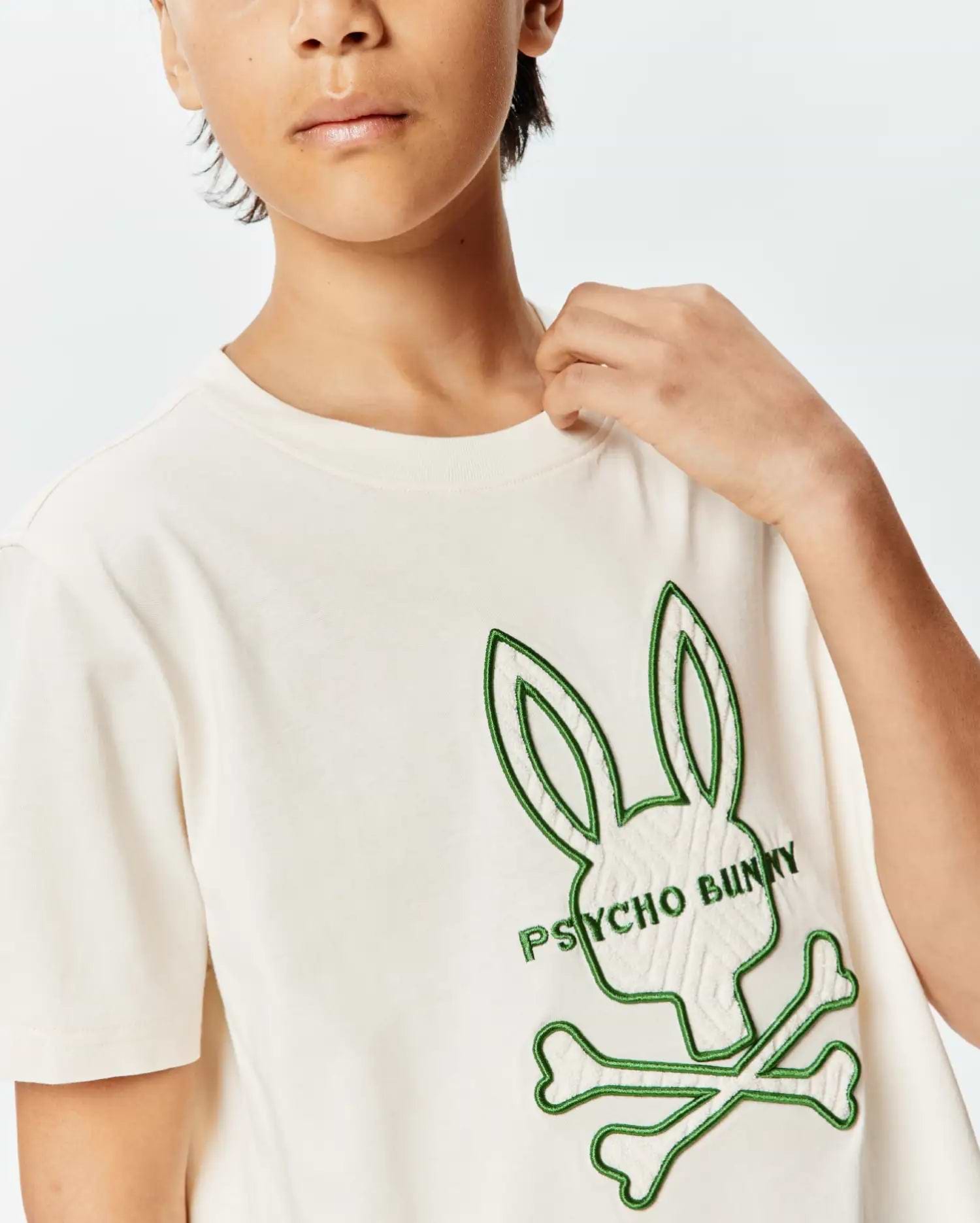 Kids Craig Graphic Tee, an off-white jersey t-shirt with a large, textured cream and green embroidered Psycho Bunny skull logo on the chest, featuring green outline and green text.