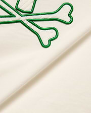 Cream Kids Craig Graphic Tee featuring a prominent green-outlined, white terry cloth embroidered Psycho Bunny skull and crossbones logo on soft jersey fabric.
