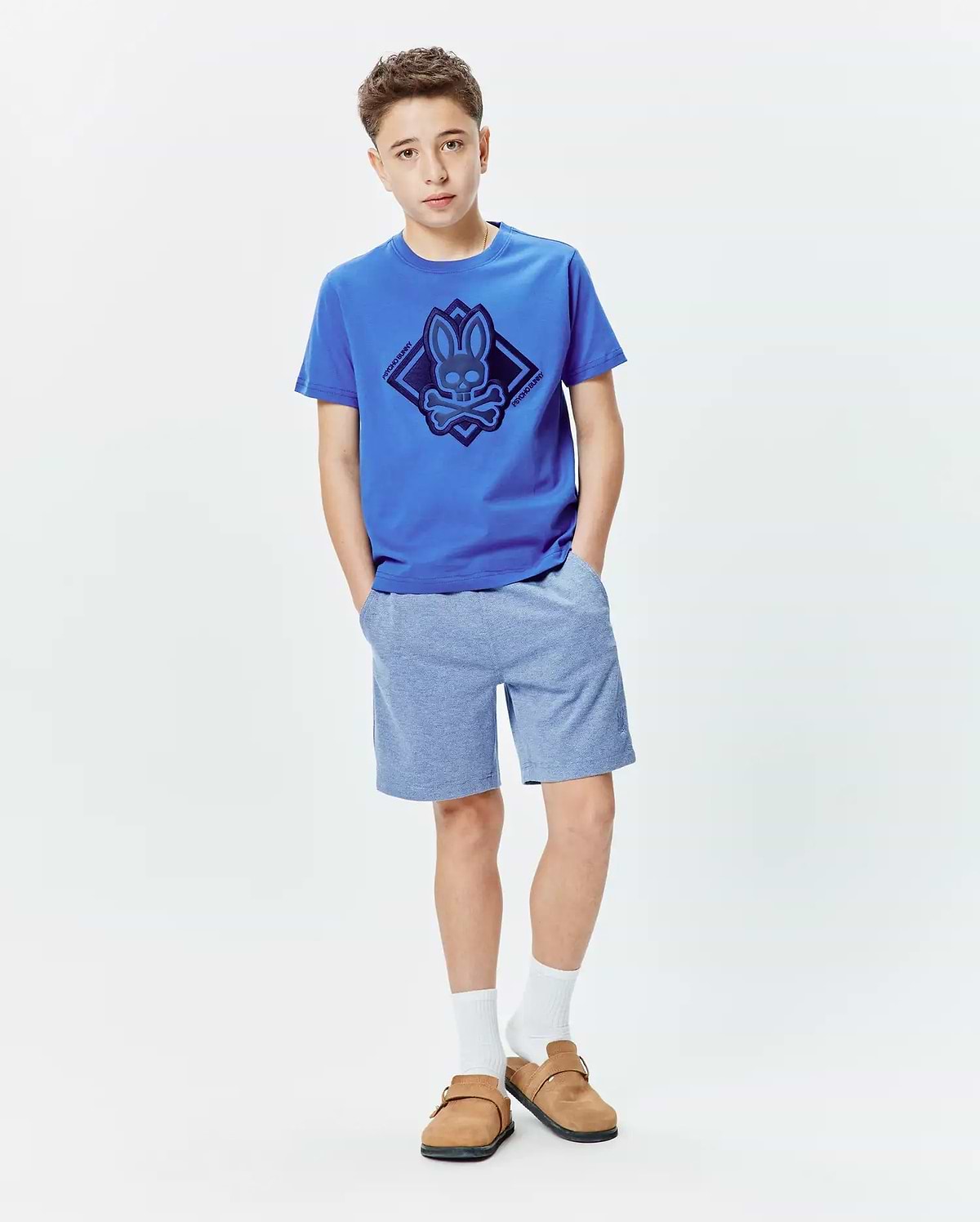 Kids Tobias Graphic Tee in royal blue jersey with a large dark blue Psycho Bunny skull and crossbones diamond graphic on the chest, paired with heather light blue jersey shorts.