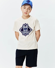 Kids Tobias Graphic Tee, a classic fit cream jersey t-shirt with a large central dark blue Psycho Bunny skull and crossbones logo graphic in a diamond shape.