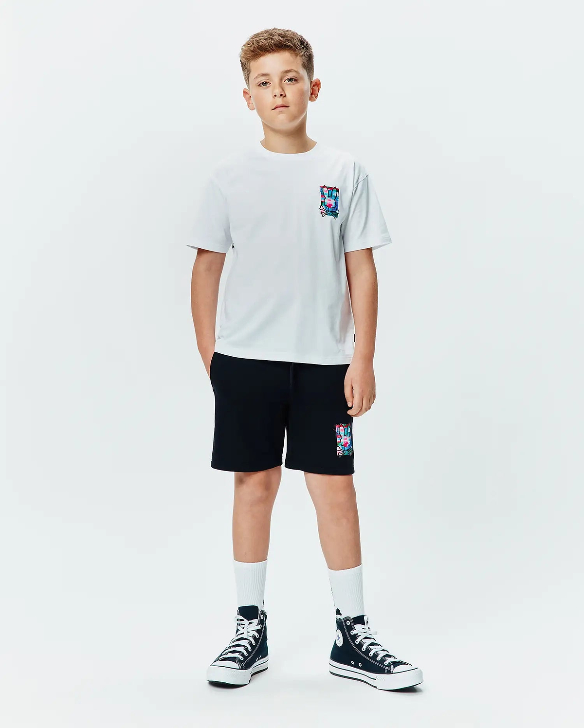 Kids Isaac Relaxed Fit Tee in white jersey with a small, colorful abstract bunny skull logo on the left chest, paired with black french terry shorts featuring a larger matching logo.