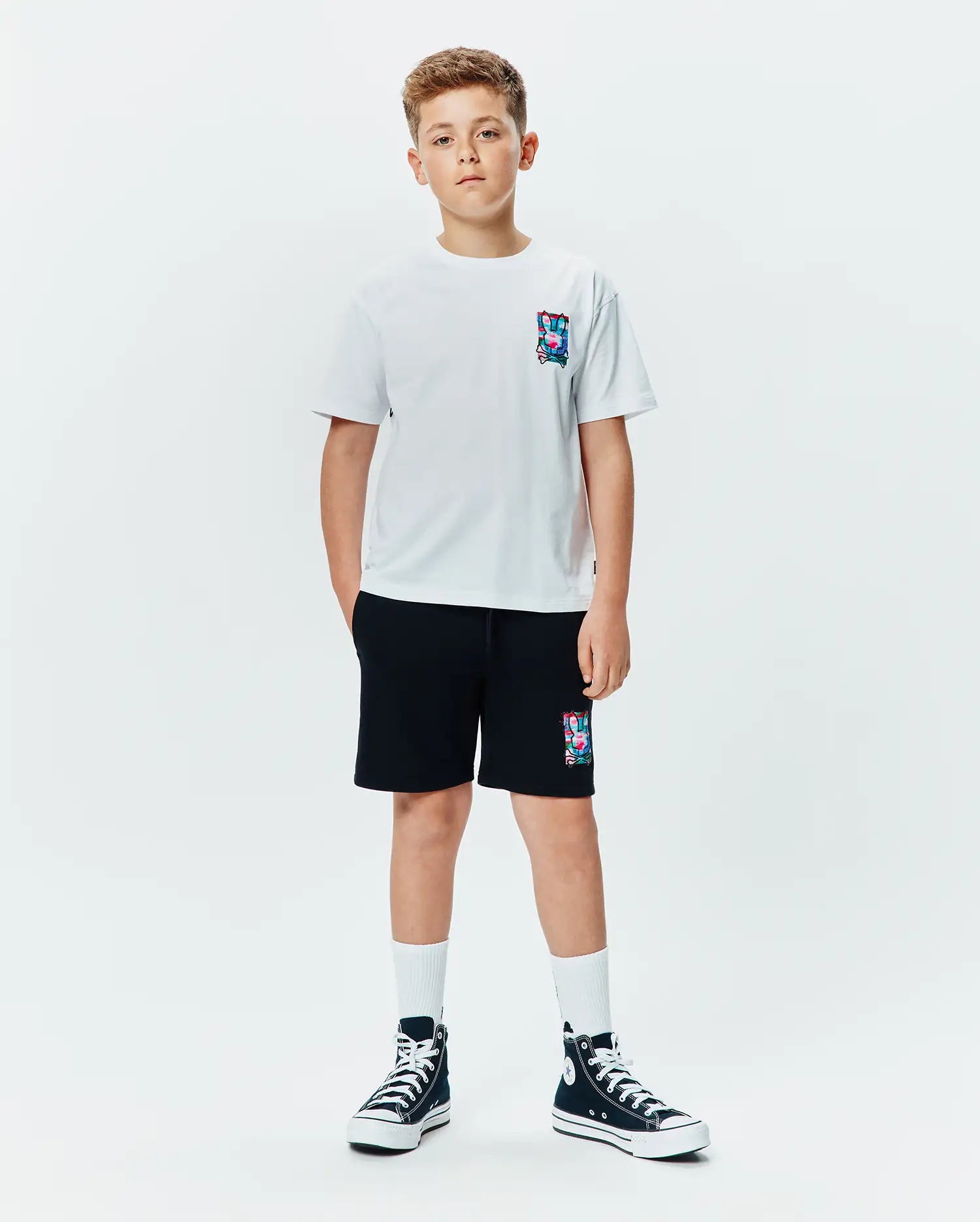 Kids Isaac Relaxed Fit Tee in white jersey with a small, colorful abstract bunny skull logo on the left chest, paired with black french terry shorts featuring a larger matching logo.