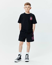Kids Duncan Relaxed Fit Tee in black jersey with a small neon pink embroidered Psycho Bunny logo on the chest, paired with black relaxed fit shorts featuring a large neon pink outline bunny skull graphic on the left leg.