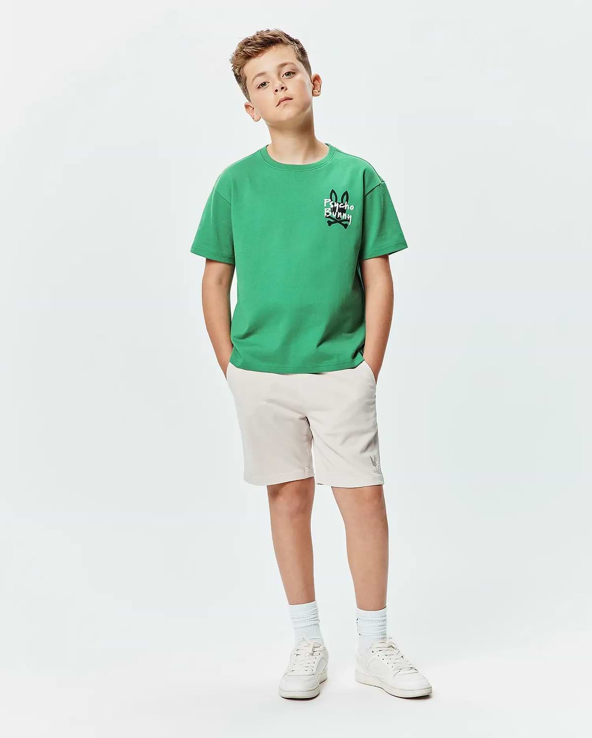Kids Duncan Relaxed Fit Tee in vibrant green jersey with a small black and white Psycho Bunny skull logo on the chest, paired with beige shorts featuring a subtle grey bunny logo.