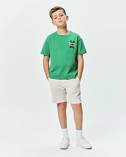 Kids Duncan Relaxed Fit Tee in vibrant green jersey with a small black and white Psycho Bunny skull logo on the chest, paired with beige shorts featuring a subtle grey bunny logo.
