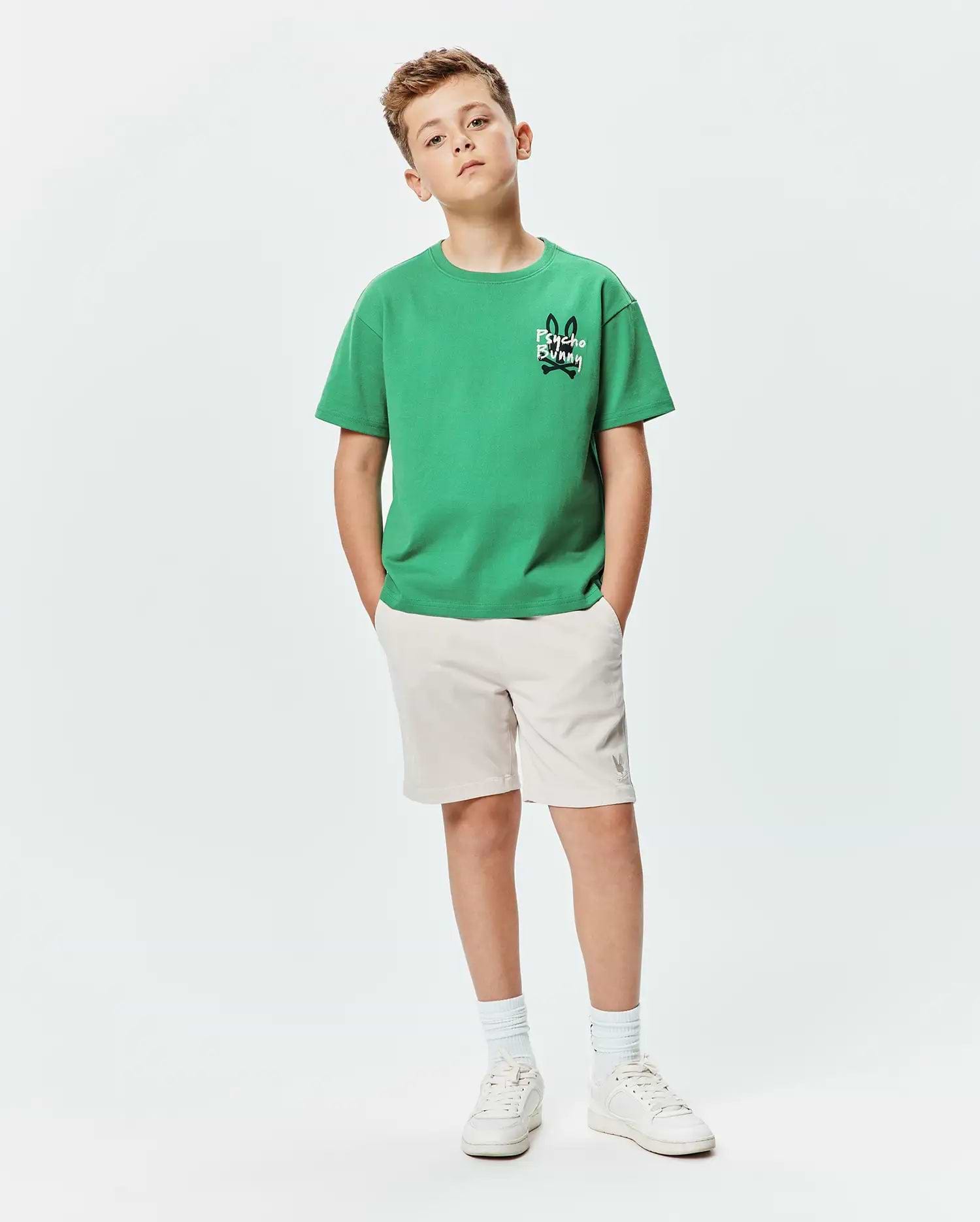 Kids Duncan Relaxed Fit Tee in vibrant green jersey with a small black and white Psycho Bunny skull logo on the chest, paired with beige shorts featuring a subtle grey bunny logo.