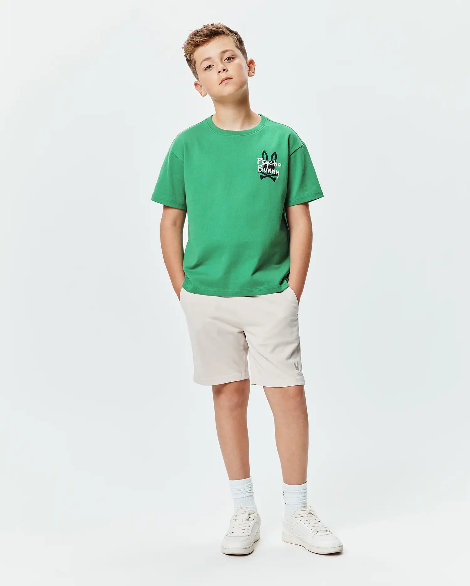 Kids Duncan Relaxed Fit Tee in vibrant green jersey with a small black and white Psycho Bunny skull logo on the chest, paired with beige shorts featuring a subtle grey bunny logo.