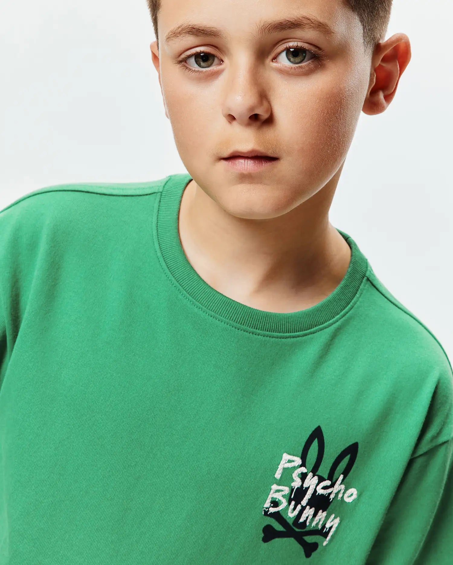 Kids Duncan Relaxed Fit Tee in vibrant green jersey, featuring a prominent distressed white and black Psycho Bunny skull logo with bunny ears and crossbones on the left chest.