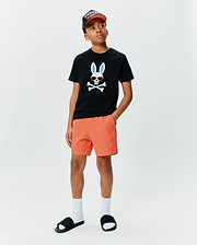 Kids Sunny Graphic Tee, a black classic fit jersey t-shirt with a large Psycho Bunny skull graphic featuring blue ears and red sunglasses on the chest, paired with orange shorts with a small embroidered bunny logo.