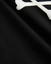 Kids Sunny Graphic Tee in black jersey knit, showcasing a large white graphic print of a bone, a key element of the iconic Psycho Bunny skull and crossbones logo.