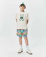 Ecru jersey Kids Sunny Graphic Tee featuring a large green Psycho Bunny skull graphic with sunglasses, complemented by multicolor all-over bunny print shorts and a white embroidered logo cap.