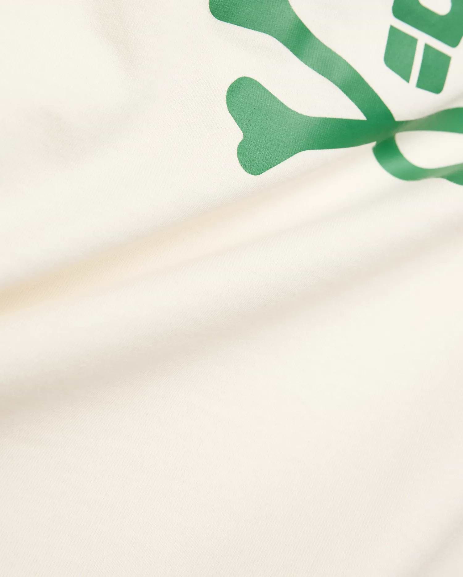Kids Sunny Graphic Tee crafted from soft cream jersey knit, showcasing a prominent, vibrant green Psycho Bunny skull and crossbones graphic print for a comfortable classic fit.