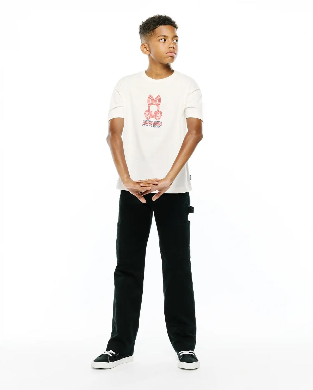 Premium cream jersey Kids Alex Relaxed Back Graphic Tee, featuring a bold red iconic Psycho Bunny skull logo and repeated text graphic on the center chest for refined streetwear style.