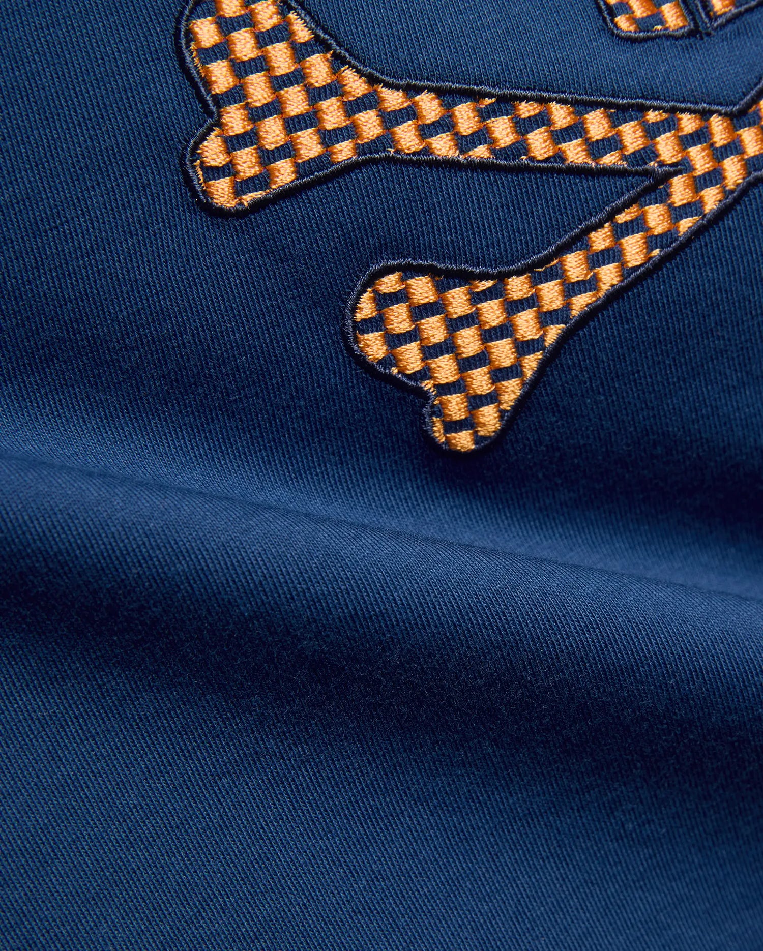Kids Stan Graphic Tee in navy blue jersey fabric, featuring a large, prominent embroidered Psycho Bunny skull logo with an orange and dark blue checkered pattern.