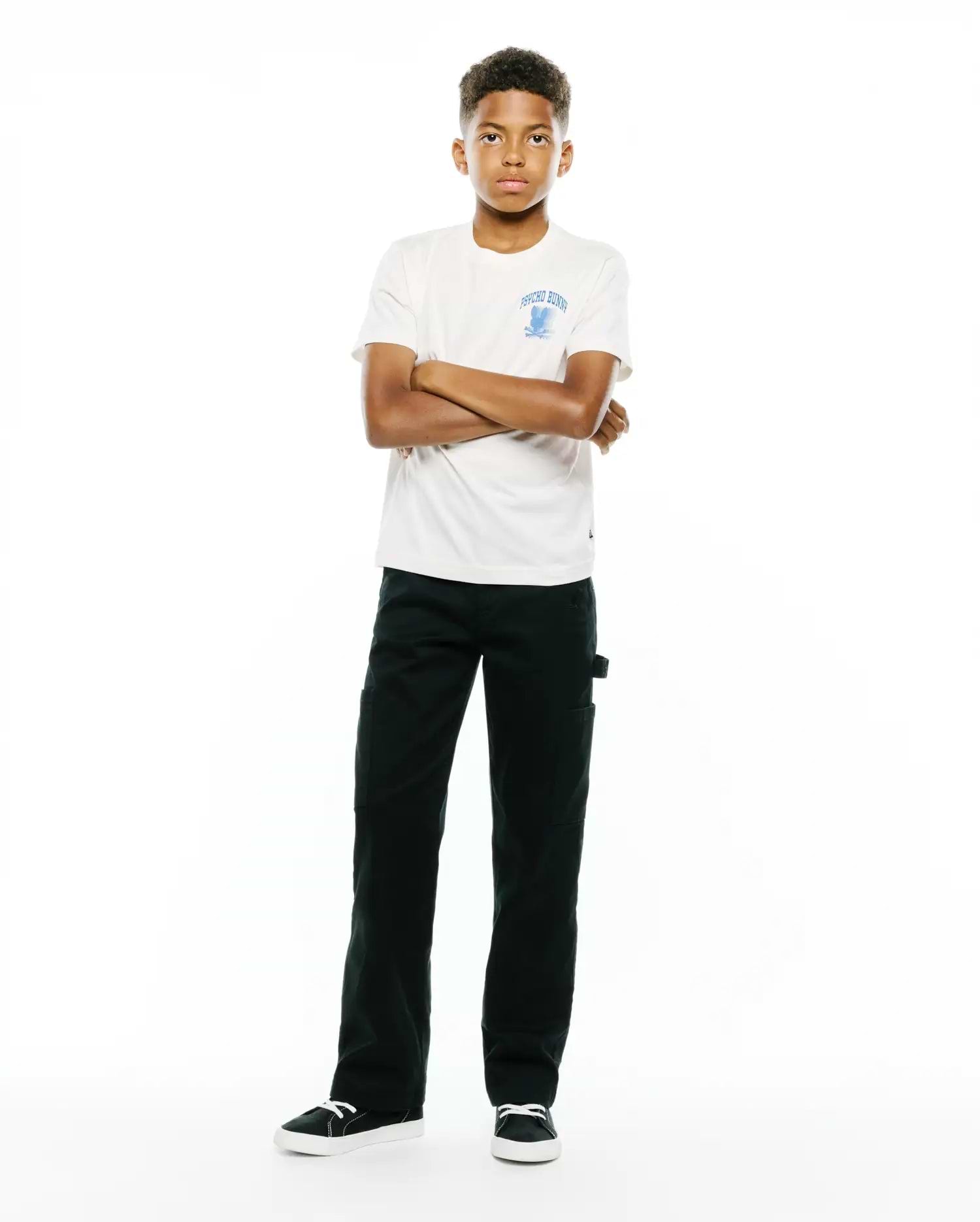 Kids Nathaniel Back Graphic Tee in off-white jersey, classic fit, featuring a light blue Psycho Bunny skull logo and text on the left chest, paired with dark green straight-leg pants.